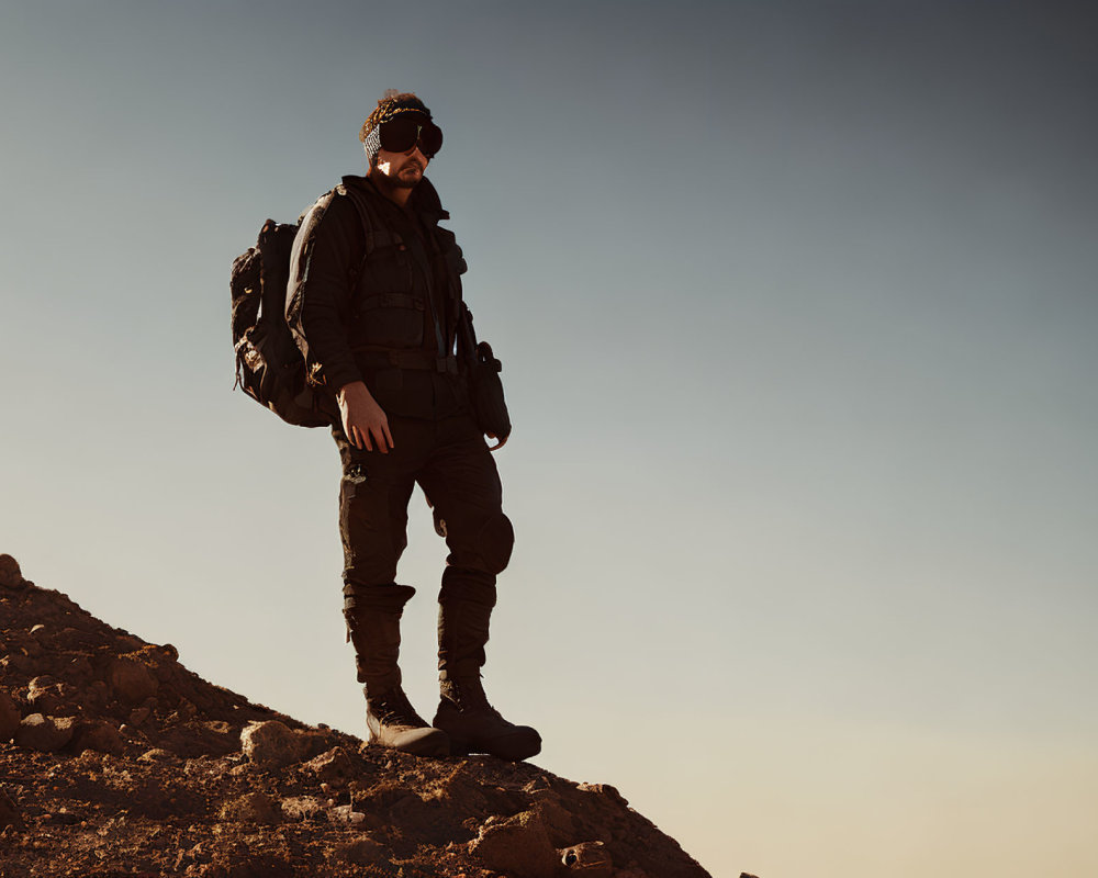 Hiker with sunglasses and backpack on rocky terrain at dusk or dawn