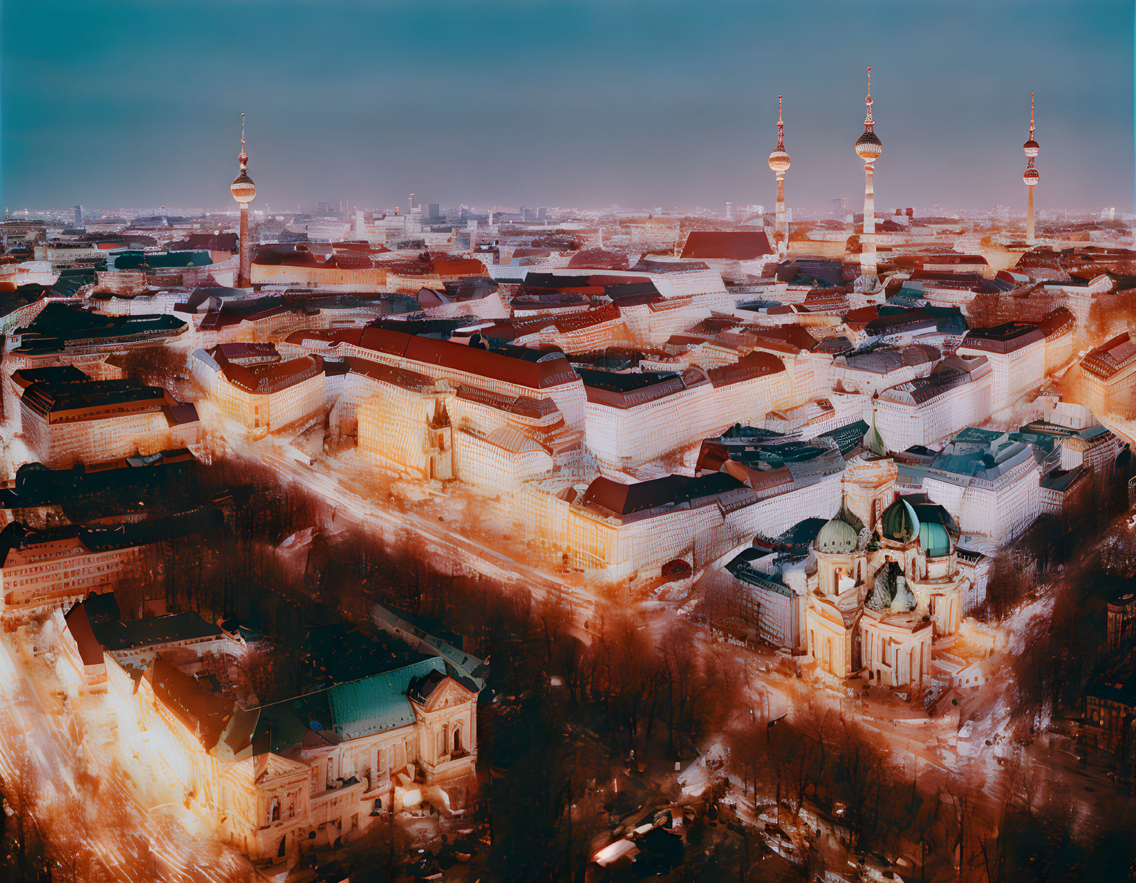 Snow-covered cityscape at twilight with illuminated cathedrals and towers.