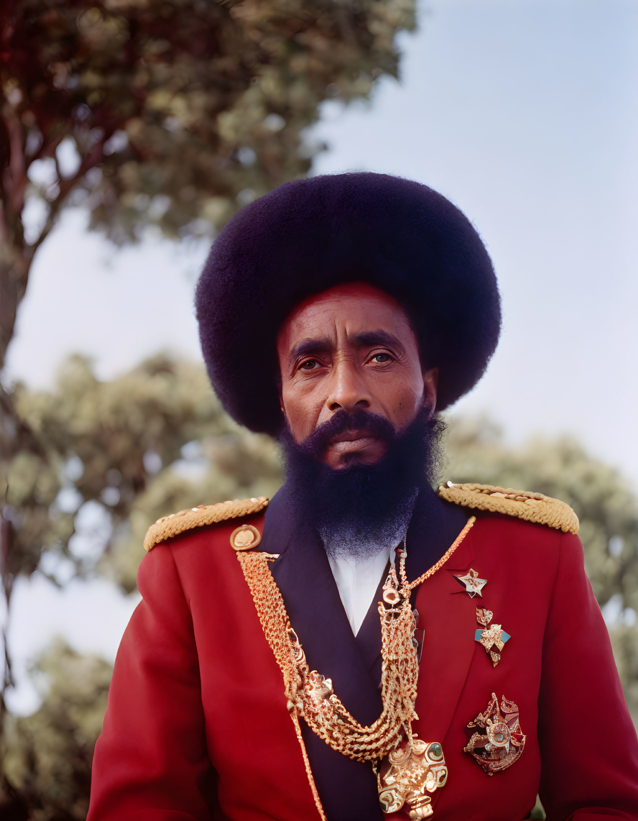 Prominent bearded man in red military uniform with medals and gold chains