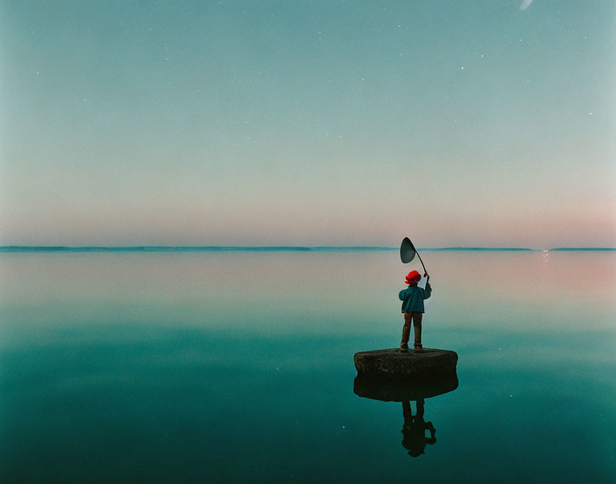 Person standing on rock with canoe paddle in calm water at dusk