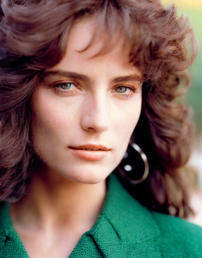 Portrait of woman with curly brown hair and blue eyes in green top with hoop earrings