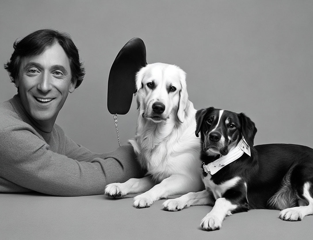 Man smiling with two dogs in studio setting, one with black ear prop.