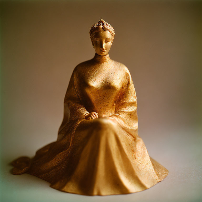 Golden seated woman figurine with flowing dress on soft-focus background