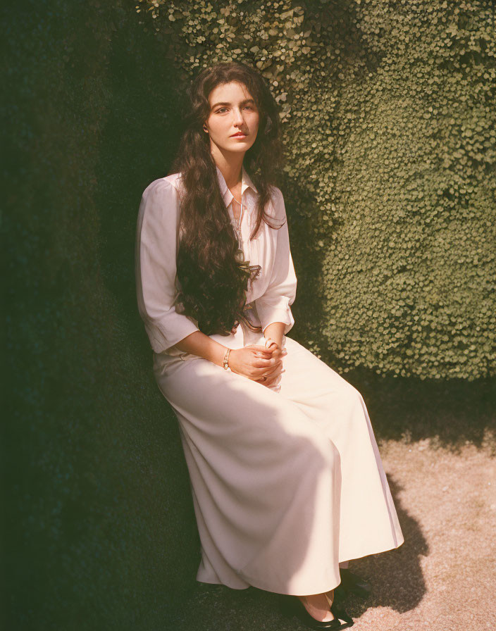 Elegant woman in thoughtful pose against hedge backdrop