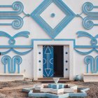 Taupe-coated person admires ornate blue and white building with intricate designs and central blue door