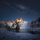 Medieval castle and village under starry night sky with snow.