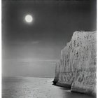 Scenic full moon over cliff by calm sea at night