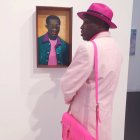 Fashionable individual in pastel suit admires portrait of man with matching style in art gallery