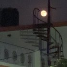 Surreal night scene with spiral staircase to moon, dark sphere, and silhouetted trees