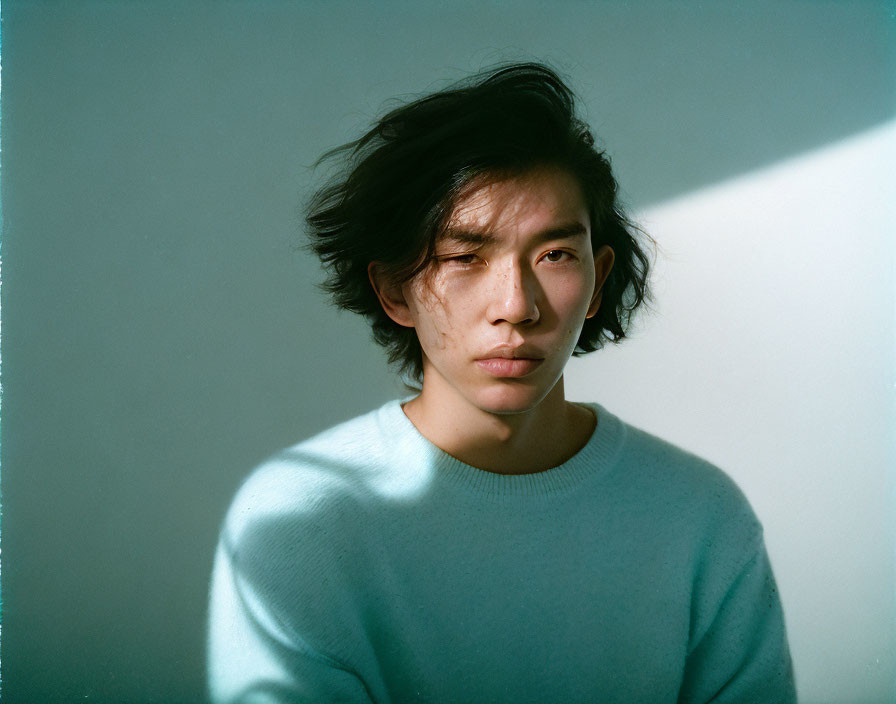 Tousled hair person in light blue sweater gazes with shadow and light.