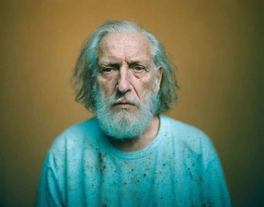 Elderly man with beard in blue shirt on orange background