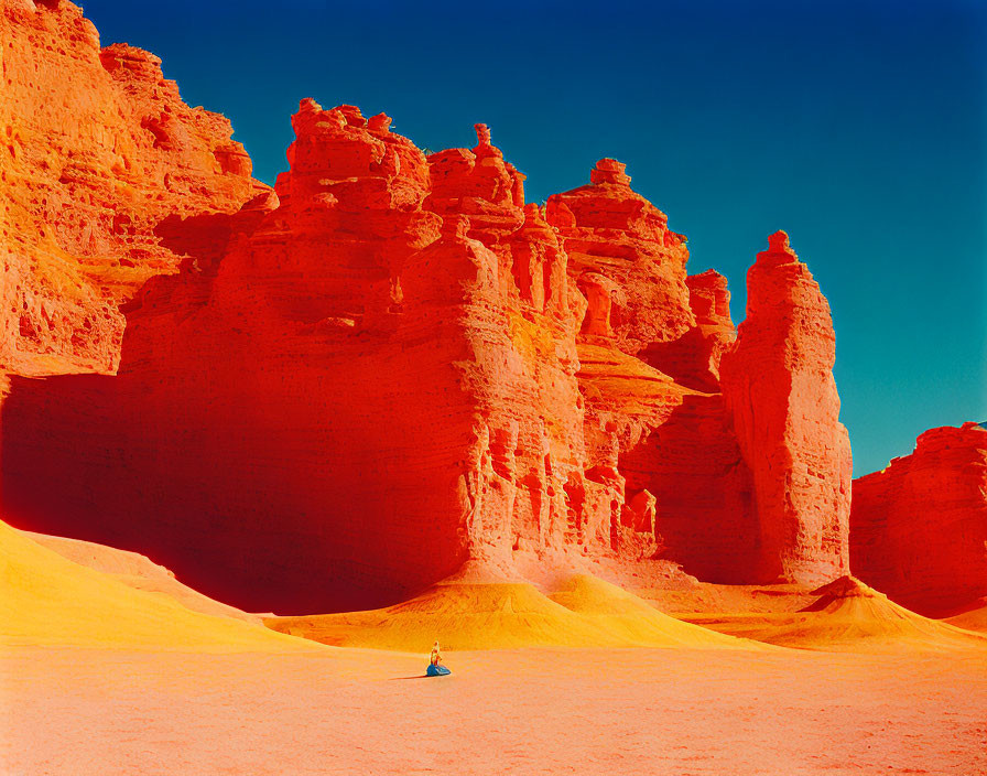 Majestic red and orange sandstone formations with figure on yellow sand dune