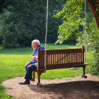 Elderly person sitting on wooden swing in peaceful park surrounded by greenery