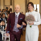 Men in white and brown suits with flowers at outdoor event among eclectic guests in forest