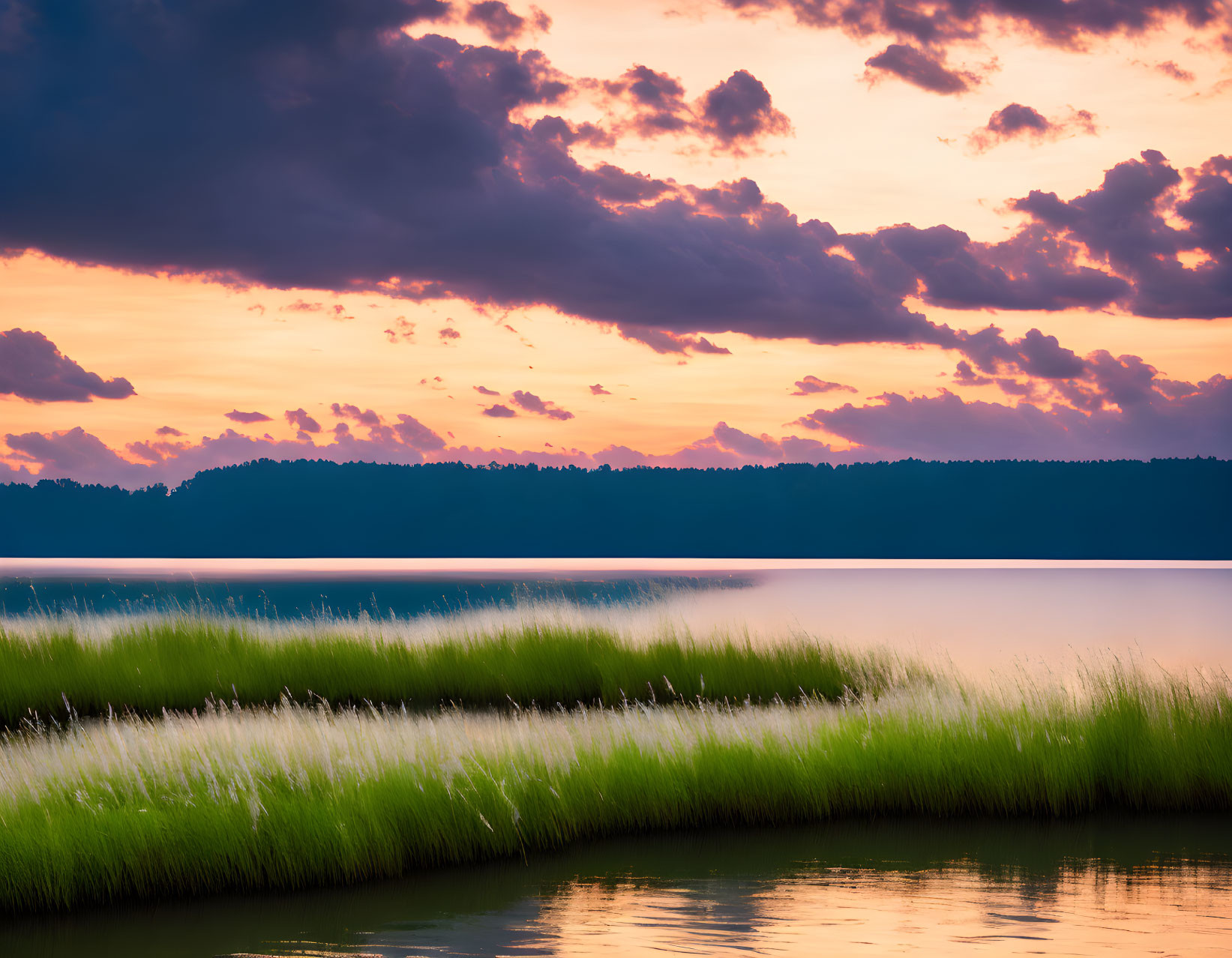 Tranquil lake scene with green grass, calm waters, and vibrant sunset reflections