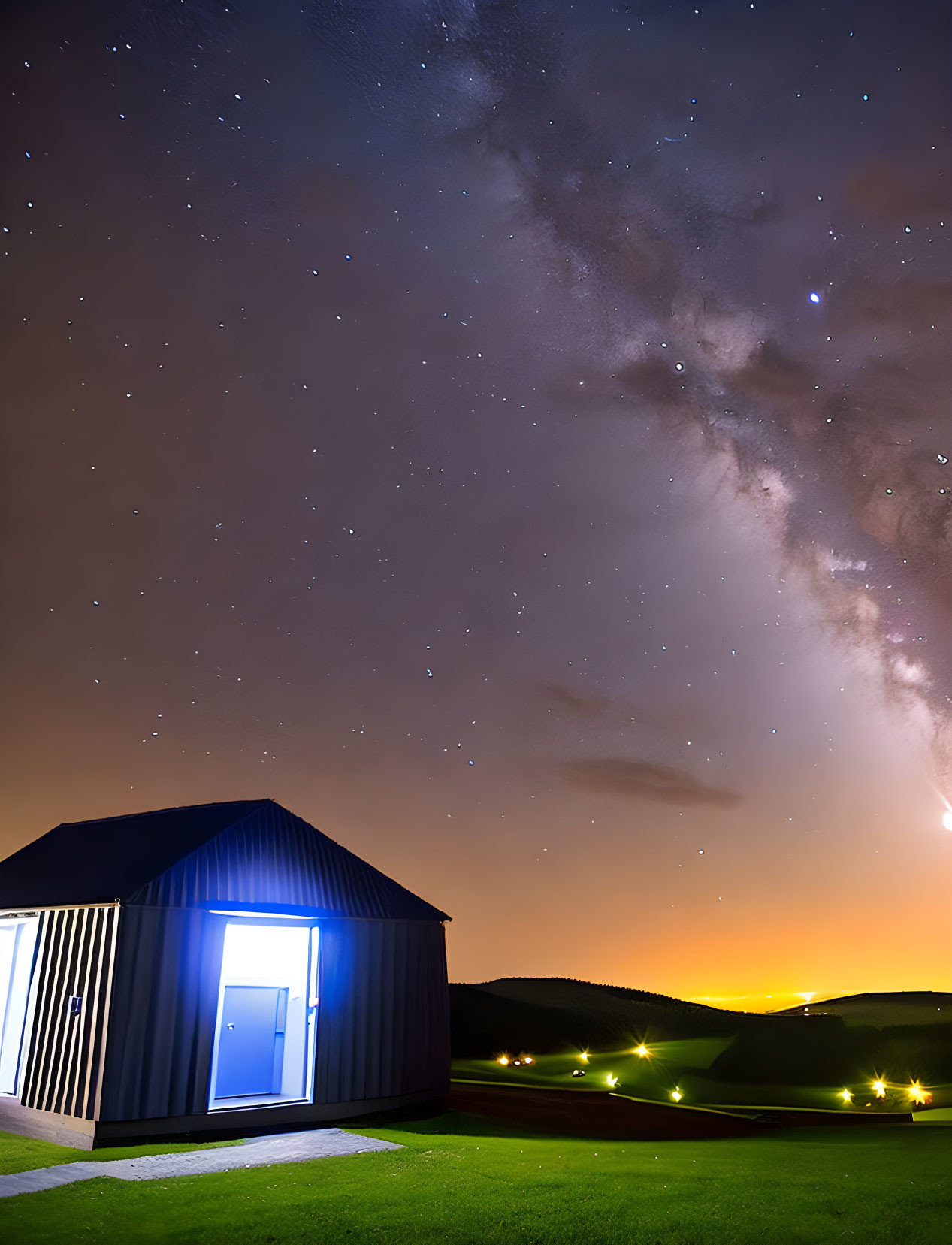 House under starry sky with Milky Way, lights on hills, warm horizon glow