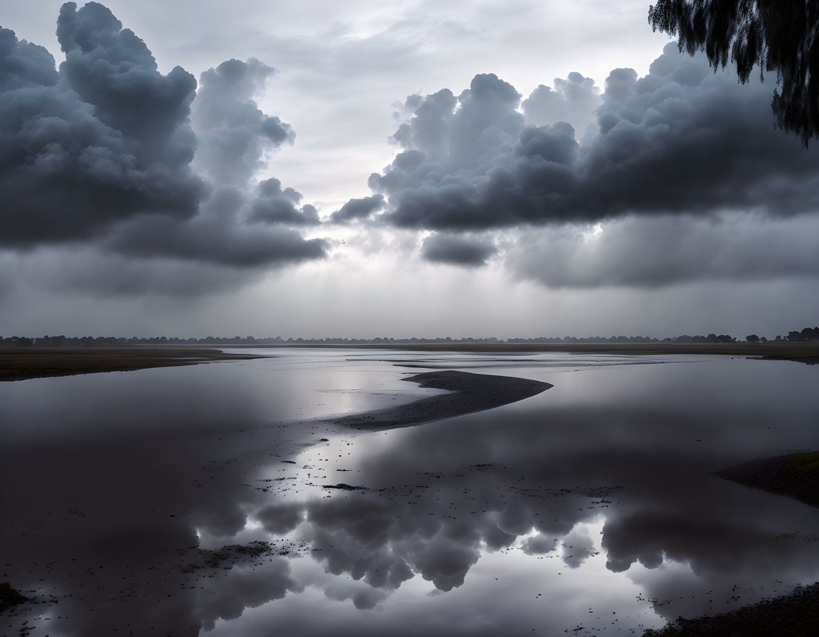 Dramatic sky with heavy clouds over serene lake and sunlight reflecting.