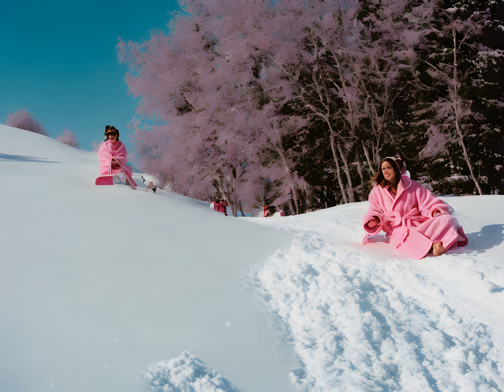 People in Pink Outfits on Snowy Hillside with Trees and Blue Sky