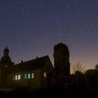 Medieval encampment with tents, central fire, castle, birds, and dramatic sky at twilight