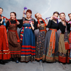 Seven women in ornate European-style dresses in misty forest.