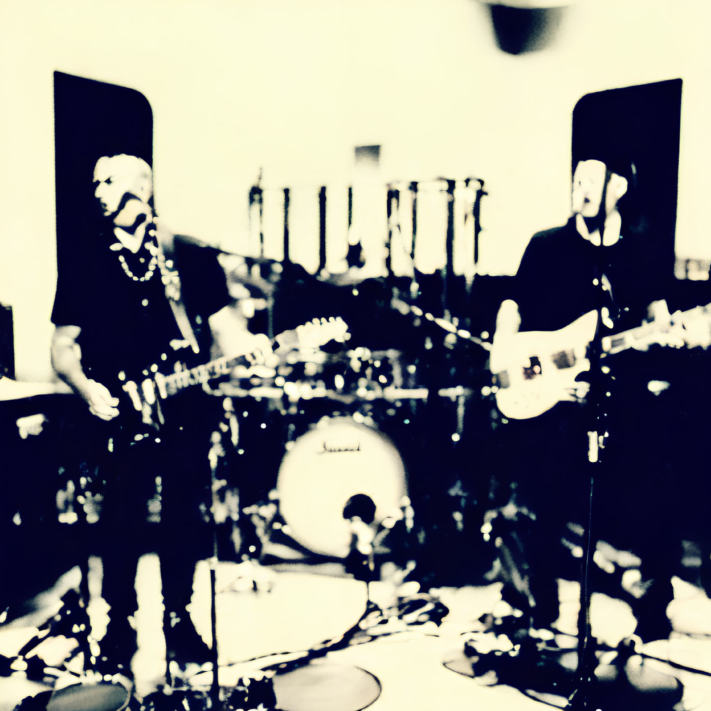 Blurred image of musicians with guitars and microphones, drum set in background