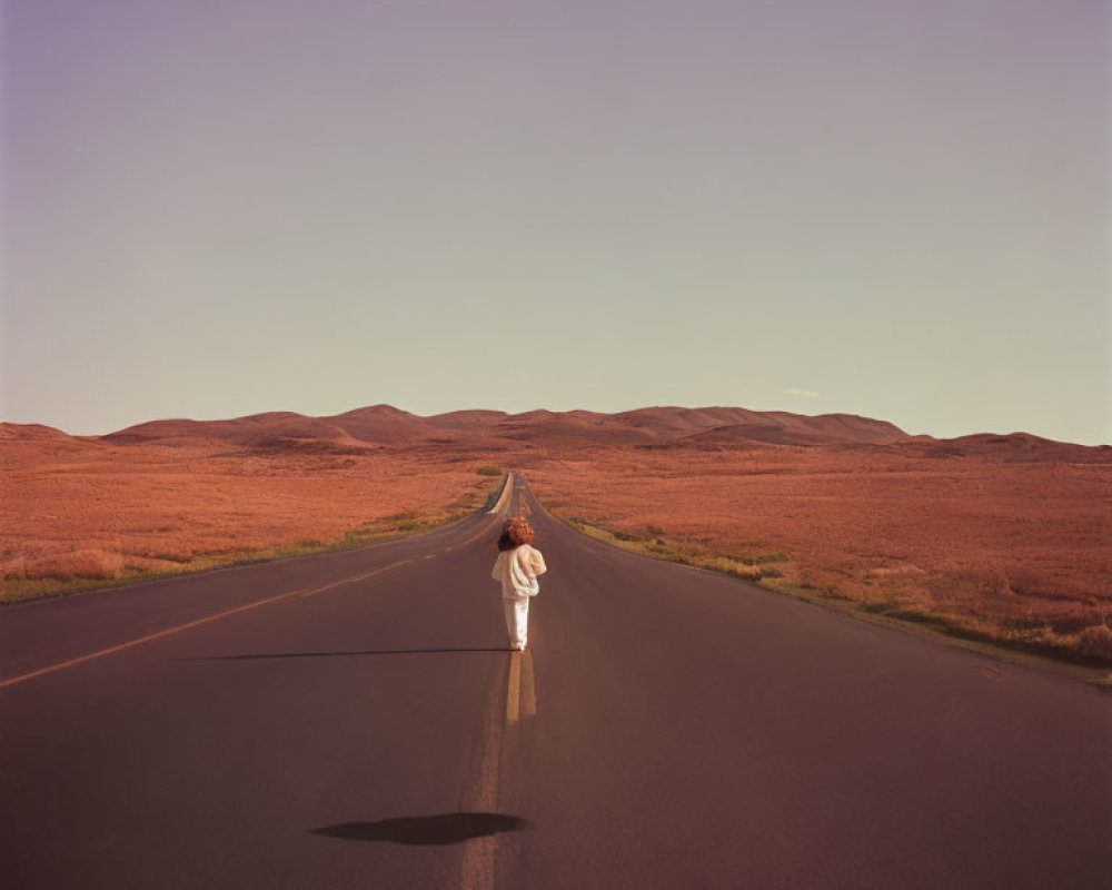 Person in White Clothing Standing on Long Straight Road in Arid Landscape at Dusk