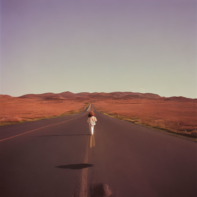 Person in White Clothing Standing on Long Straight Road in Arid Landscape at Dusk