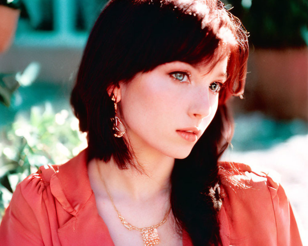 Dark-haired woman in red blouse and gold necklace gazes sideways