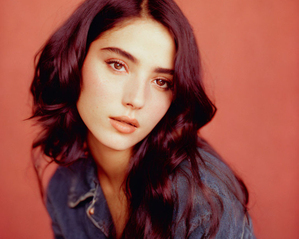 Portrait of woman with dark wavy hair and fair skin in denim jacket on red background