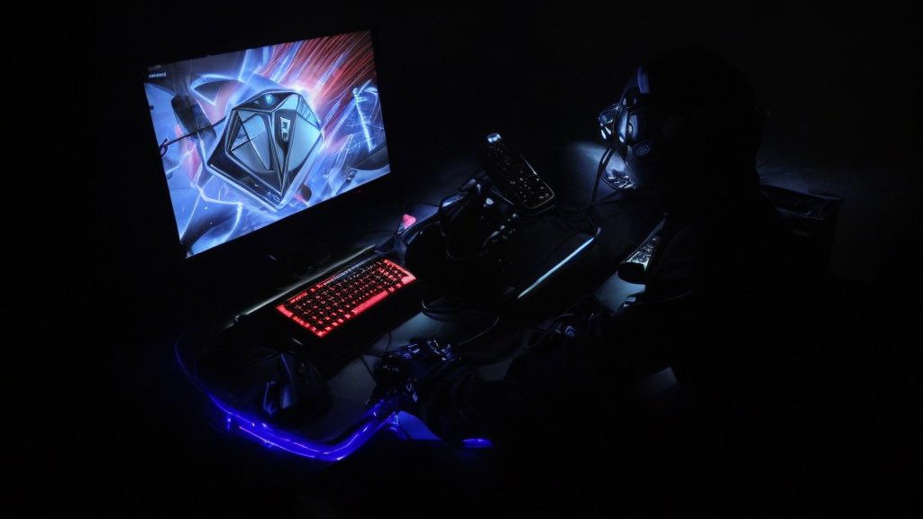 Person gaming in dark room with backlit keyboard and glowing PC case.