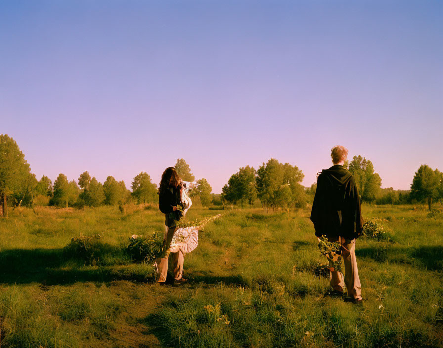 Lush Field with Two People Walking at Sunrise or Sunset