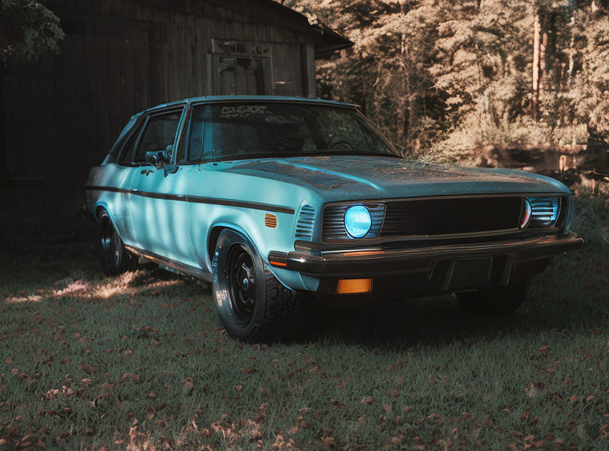 Vintage Blue Car Parked in Front of Wooden Shed with Headlight On