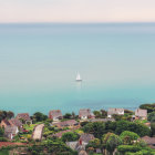 Stone houses and lighthouse in coastal village with winding paths and greenery under hazy sky