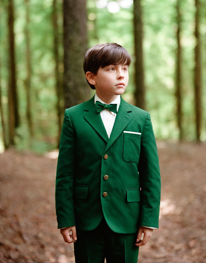 Young boy in green suit and bow tie in forest setting