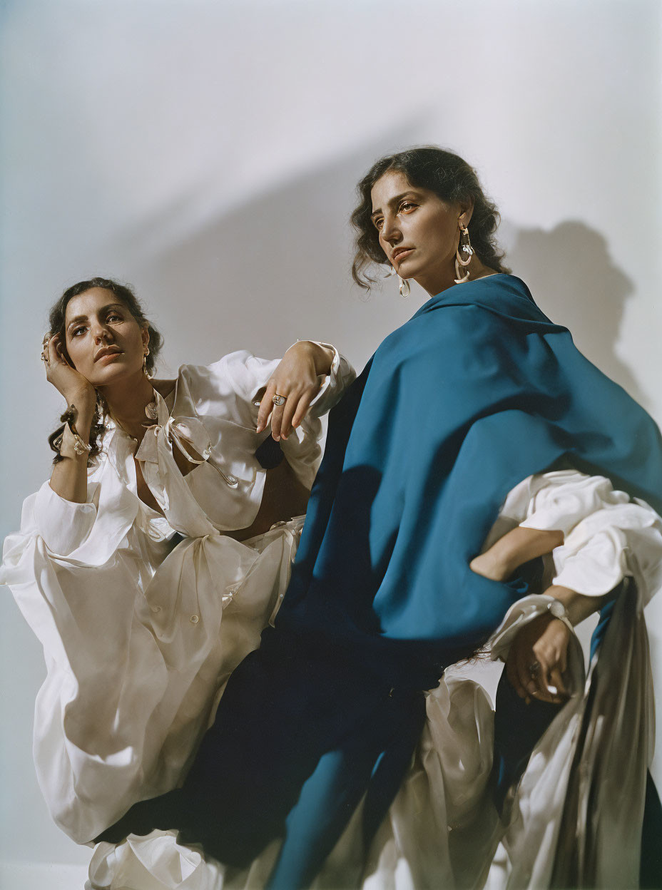 Elegant individuals in white ruffled shirt and blue garment pose on neutral backdrop