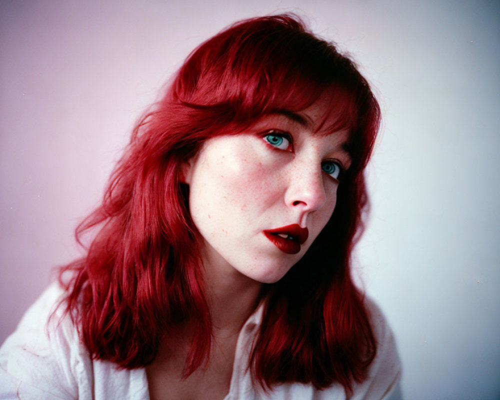 Portrait of woman with red hair, freckles, and green eyes in white shirt.