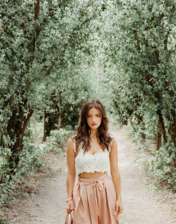 Woman in white lace top and high-waisted skirt on tree-lined path