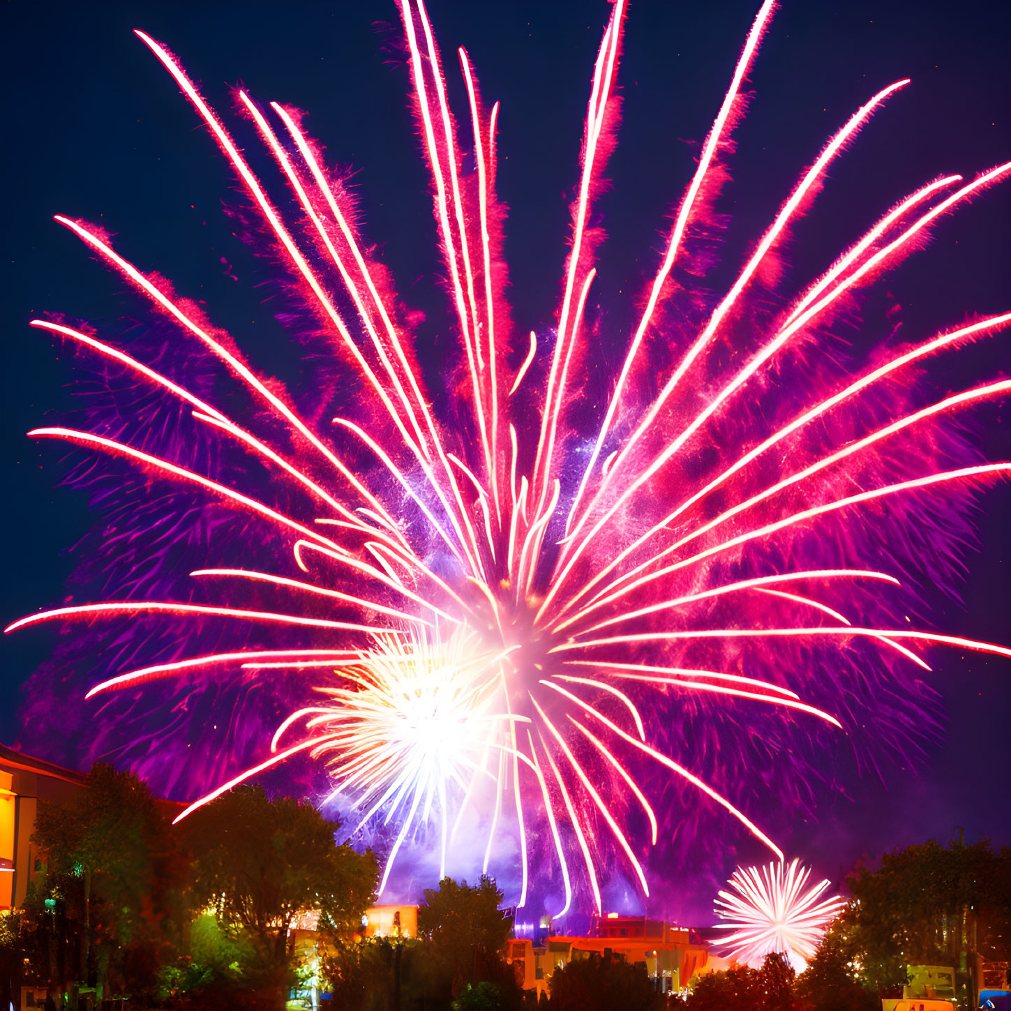 Colorful pink and white fireworks illuminate city skyline at night