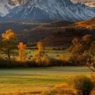 Colorful pastoral scene with hills, farm, trees, hay wagon, and figure under sunset sky