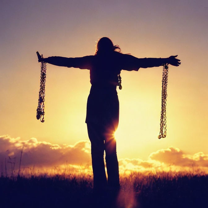 Person silhouette holding chains against sunset sky