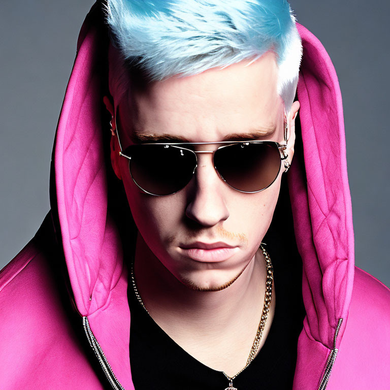 Blue-haired person in pink hoodie with aviator sunglasses and light mustache.