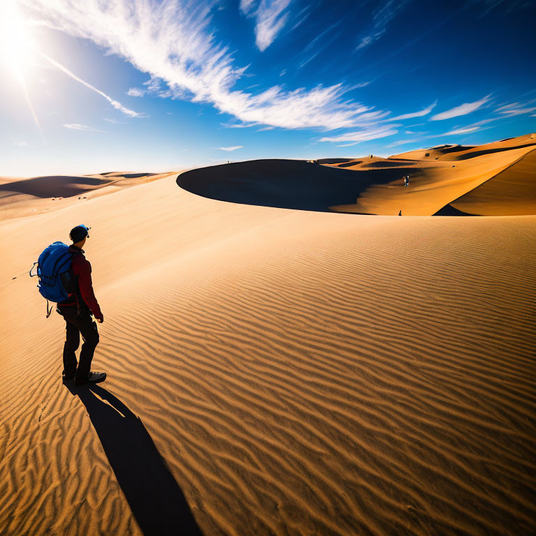 Traveler with Blue Backpack Standing on Desert Dune Under Clear Sky