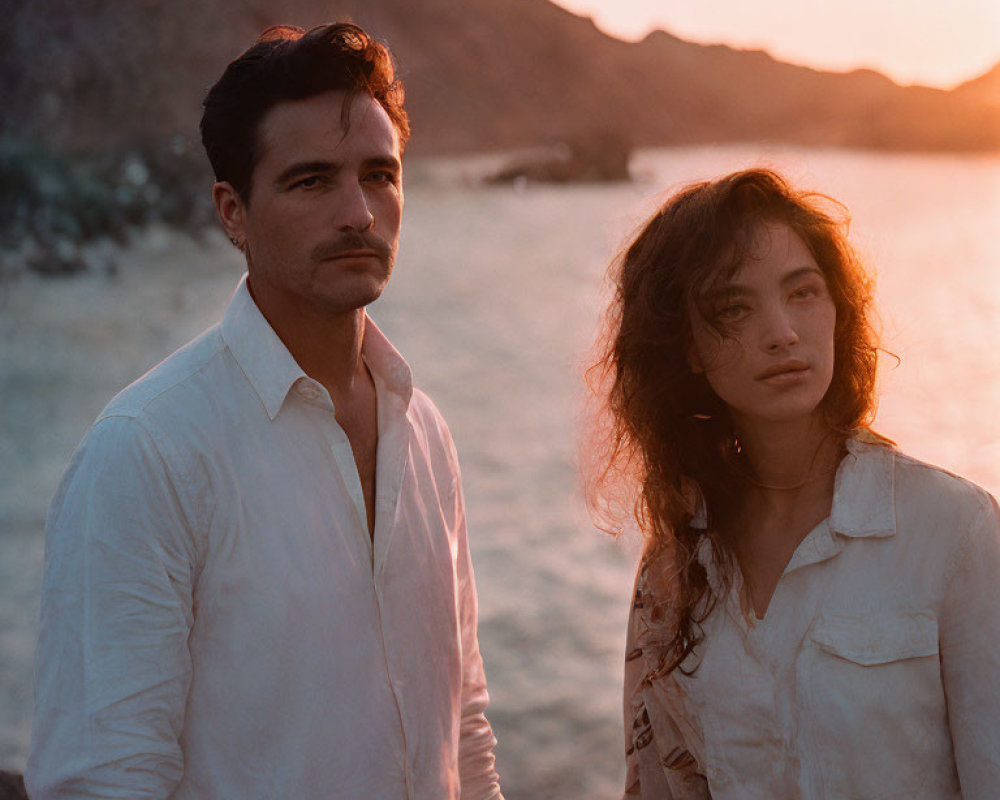 Couple standing on beach at sunset with rocky hills in background