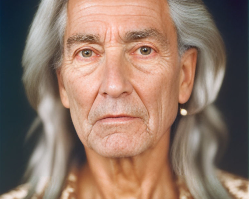 Elderly person with long grey hair and deep wrinkles in golden patterned shirt