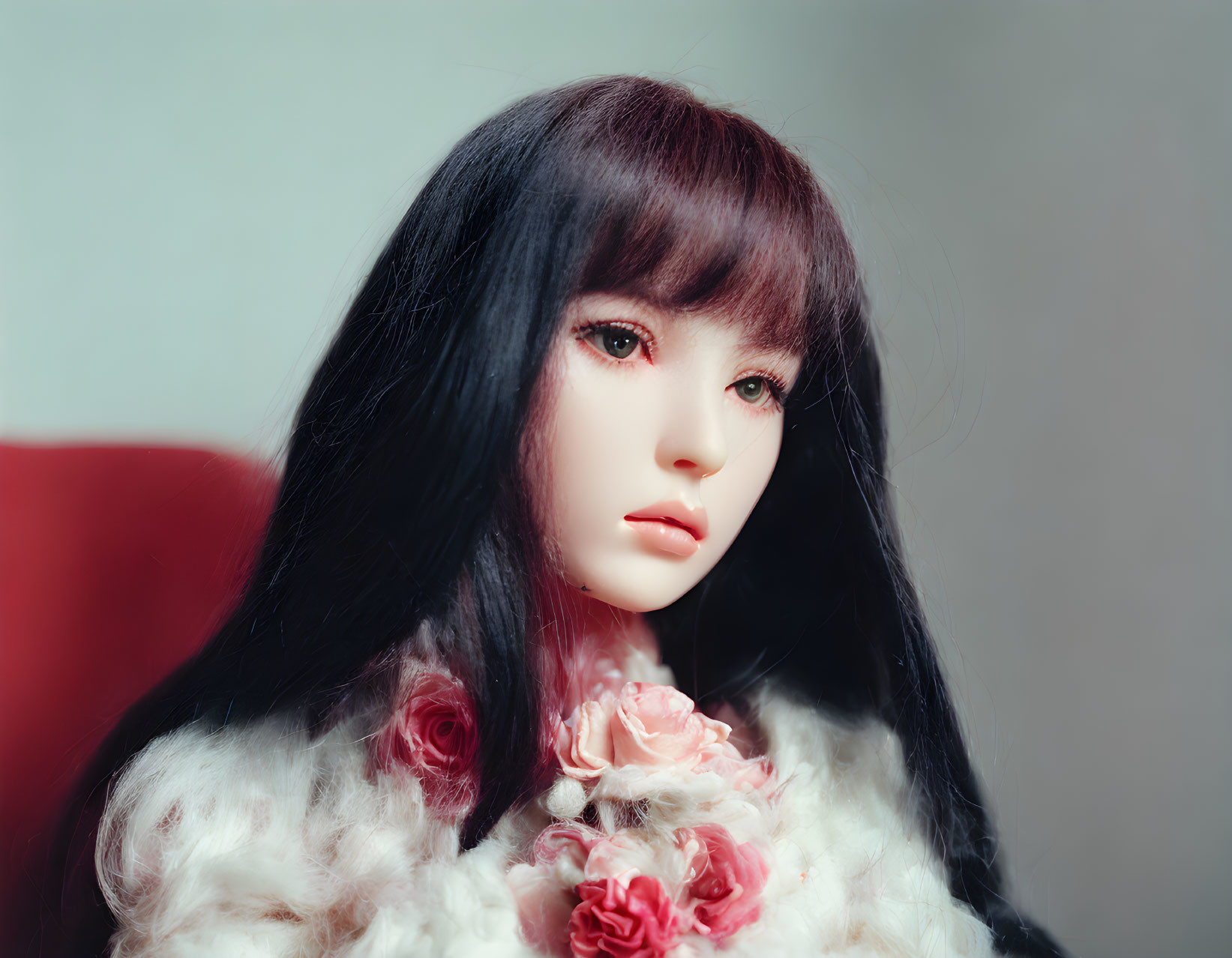 Realistic doll with black hair and red lips in white furry outfit on red background