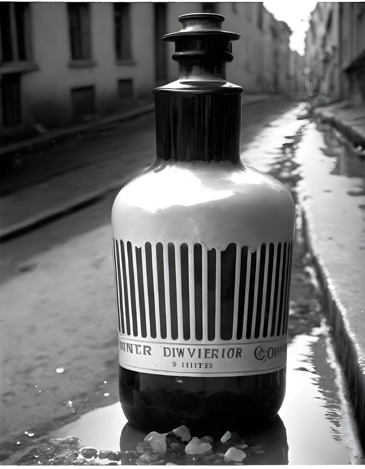 Decorative oversized bottle with label on wet street, reflecting buildings in alleyway