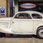 Vintage White Car Parked Beside Retro Gas Station with Blue Car