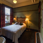 Inviting single bed with red curtains, lamps, chair, and city view.