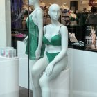 Boutique display featuring mannequins in turquoise gown and lingerie with jewelry and floral backdrop