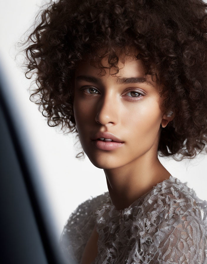 Portrait of person with curly hair, subtle makeup, and lacy top against neutral background